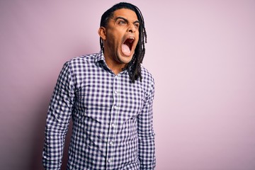 Young handsome african american afro man with dreadlocks wearing casual shirt angry and mad screaming frustrated and furious, shouting with anger. Rage and aggressive concept.