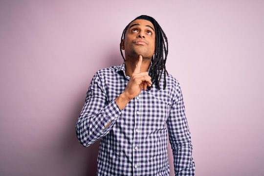 Young handsome african american afro man with dreadlocks wearing casual shirt Thinking concentrated about doubt with finger on chin and looking up wondering