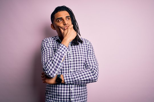 Young handsome african american afro man with dreadlocks wearing casual shirt with hand on chin thinking about question, pensive expression. Smiling with thoughtful face. Doubt concept.