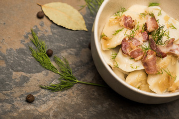 delicious varenyky with cracklings and dill in bowl near bay leaves and black peppercorns on stone...