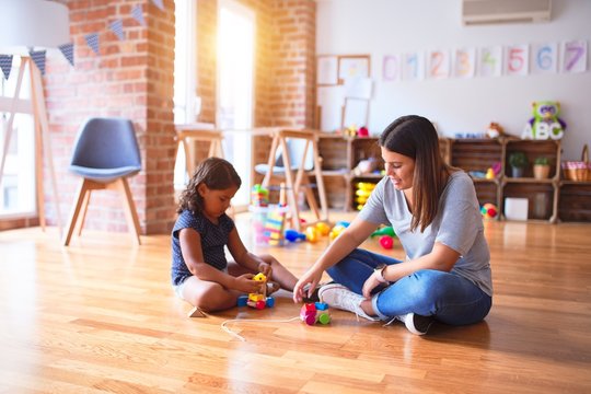 Beautiful teacher and toddler girl playing with train at kindergarten