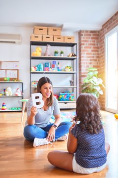 Beautiful teacher teaching alphabet to student toddler girl at kindergarten