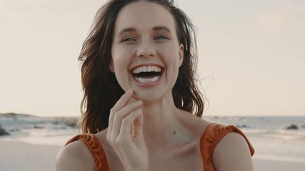 Close up of a pretty woman smiling on the beach. Female model looking at camera and laughing with hand on her face. - Powered by Adobe