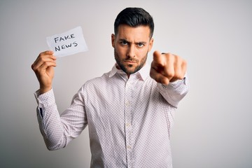 Young business man holding fake news paper over isolated background pointing with finger to the camera and to you, hand sign, positive and confident gesture from the front