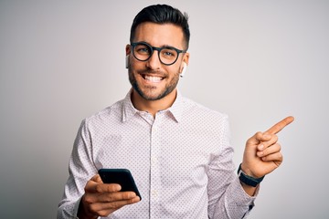 Young handsome man wearing glasses having conversation using smartphone and earphones very happy pointing with hand and finger to the side