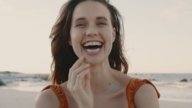Close up of a pretty woman smiling on the beach. Female model looking at camera and laughing with hand on her face.
