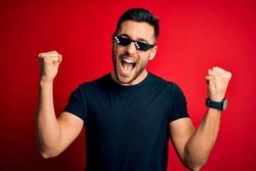 Young handsome man wearing funny thug life sunglasses over isolated red background celebrating...