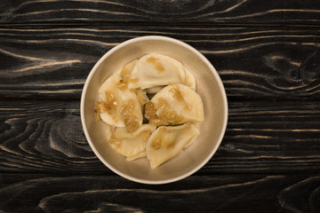 top view of delicious varenyky with fried onion in bowl on black wooden table