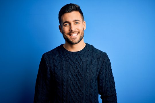 Young handsome man wearing casual sweater standing over isolated blue background with a happy and cool smile on face. Lucky person.