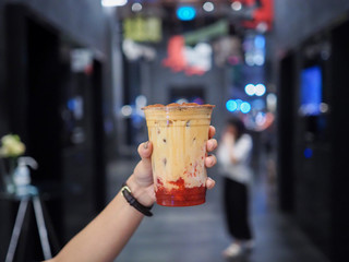 Hand holds a plastic glass of iced coffee latte with layer of jam strawberry. selective focus.