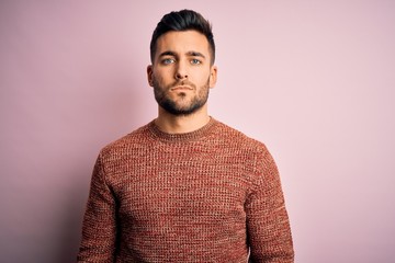Obraz premium Young handsome man wearing casual sweater standing over isolated pink background with serious expression on face. Simple and natural looking at the camera.
