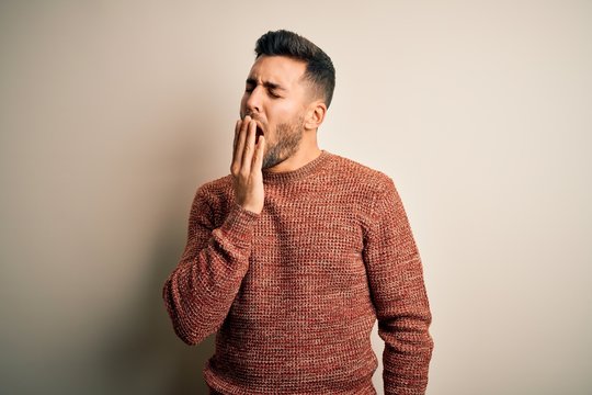 Young handsome man wearing casual sweater standing over isolated white background bored yawning tired covering mouth with hand. Restless and sleepiness.