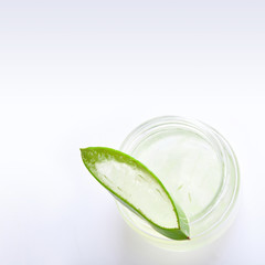 Close up bottle of aloe vera gel with sliced aloe vera leaf on white background, top view. Skincare, health, beauty and spa concept.