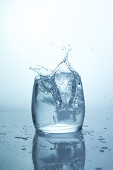 Large splash of water with bubbles, falling ice cube in a glass of water, single stack on a light background water splash