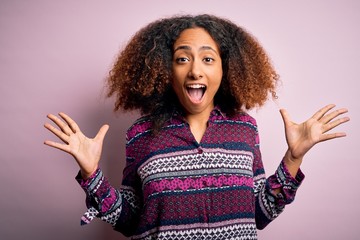 Young african american woman with afro hair wearing colorful shirt over pink background celebrating crazy and amazed for success with arms raised and open eyes screaming excited. Winner concept