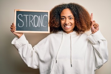 Young african american woman with afro hair holding blackboard with strong message surprised with an idea or question pointing finger with happy face, number one