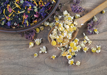 dried chamomile flowers in a wooden spoon, blended tea in a bowl and thyme on a wooden table....