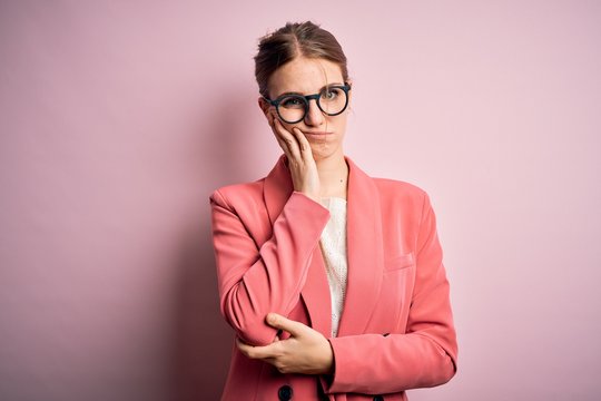 Young beautiful redhead woman wearing jacket and glasses over isolated pink background thinking looking tired and bored with depression problems with crossed arms.
