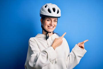 Young beautiful redhead cyclist woman wearing bike helmet over isolated blue background smiling and looking at the camera pointing with two hands and fingers to the side.