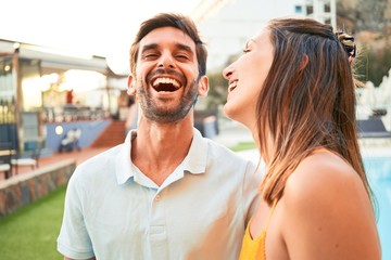 Young beautiful couple on vacation smiling happy and confident. Standing with smile on face hugging at the beach club