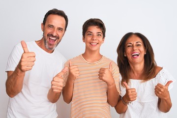 Family of three, mother, father and son standing over white isolated background success sign doing positive gesture with hand, thumbs up smiling and happy. Cheerful expression and winner gesture.