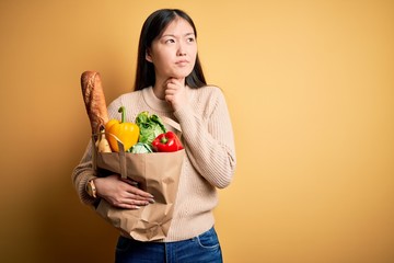 Young asian woman holding paper bag of fresh healthy groceries over yellow isolated background Touching painful neck, sore throat for flu, clod and infection