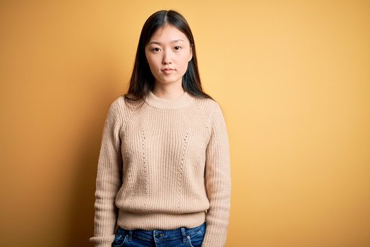 Young beautiful asian woman wearing casual sweater over yellow isolated background Relaxed with serious expression on face. Simple and natural looking at the camera.