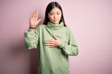 Young beautiful asian woman wearing green winter sweater over pink solated background Swearing with...