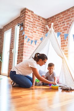 Beautiful teacher and toddler boy sitting on the floor playing inside  tipi at kindergarten