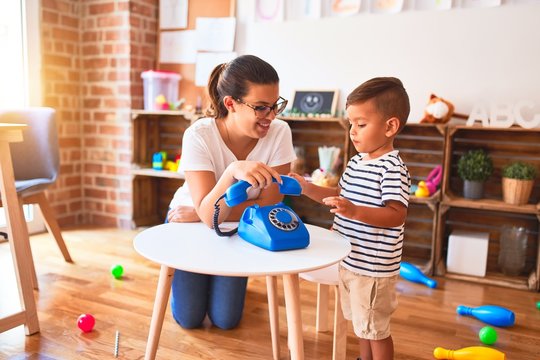 Beautiful teacher and toddler boy playing with vintage blue phone at kindergarten