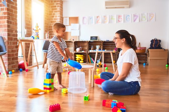 Beautiful teacher and toddler boy playing drum using skitlle and plastic basket at kindergarten