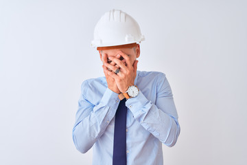 Young business man wearing contractor safety helmet over isolated background with sad expression covering face with hands while crying. Depression concept.