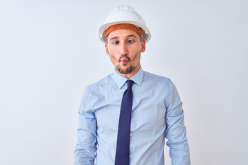Young business man wearing contractor safety helmet over isolated background making fish face with lips, crazy and comical gesture. Funny expression.