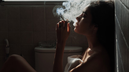 Asian woman inhaling and cigarette vaping. Female secretly smoking in bathroom at home. Concept of quit smoking and anti cigarette.