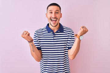 Fototapeta premium Young handsome man wearing nautical striped t-shirt over pink isolated background celebrating surprised and amazed for success with arms raised and open eyes. Winner concept.