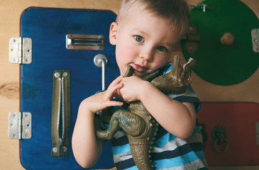 Portrait of cute little child boy hugging toy dinosaur on busyboard background. Kid in...