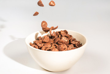 Chocolate corn flakes falling to the white bowl isolated on white. Motion.