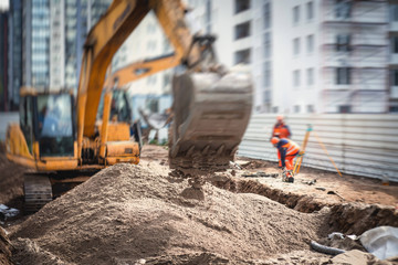 Yellow heavy excavator excavating sand and working during road works, unloading sand during construction of the new road