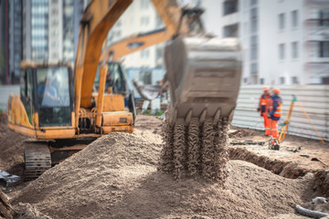 Yellow heavy excavator excavating sand and working during road works, unloading sand during...
