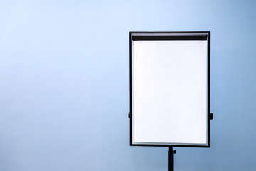 Flip chart board with a blank sheet of paper on a light blue wall background. Blank image on the education theme with copy space.