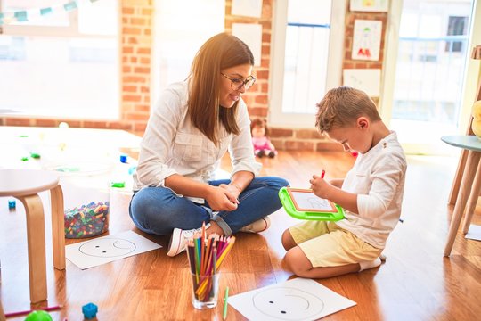 Beautiful teacher and toddler drawing using digital board around lots of toys at kindergarten