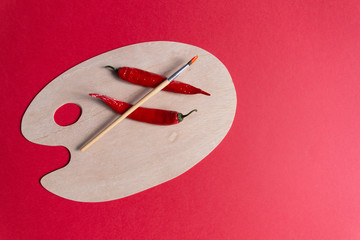 Artist brush and hot chilli peppers on wooden clean palette on red background