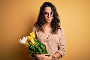 Young beautiful romantic woman with curly hair holding bouquet of yellow tulips skeptic and nervous, frowning upset because of problem. Negative person.