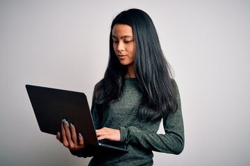 Naklejka premium Young beautiful chinese woman using laptop standing over isolated white background with a confident expression on smart face thinking serious