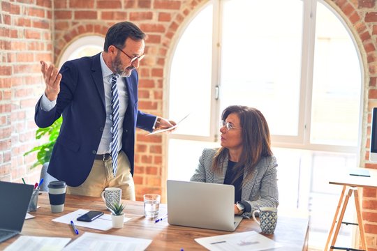 Two middle age business workers working together. Man bullying woman at the office