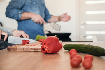 Handsome man cutting vegetables on wooden chopping board at kitchen counter.