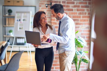 Two middle age business workers smiling happy and confident. Working together with smile on face using laptop at the office