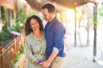 Obraz premium Middle age beautiful couple smiling happy and confident at town park. Standing with smile on face and hugging