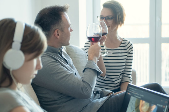 Sad Little Child Listening To Music Alone While Addicted Parents Drinking Alcohol At Home. Family Alcoholism Problem Concept