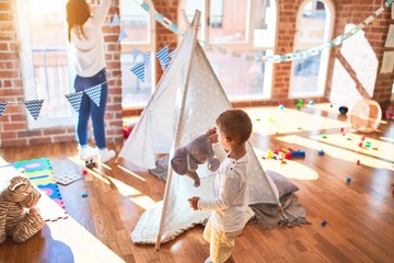 Beautiful teacher and toddler playing inside tipi around lots of toys at kindergarten